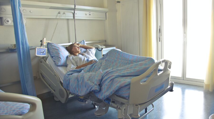 A female patient lies in a hospital bed, looking out the window.