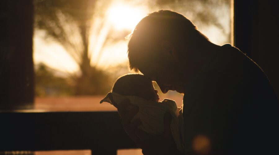 A silhouette of a man and his new born child are seen against a sunny backdrop.