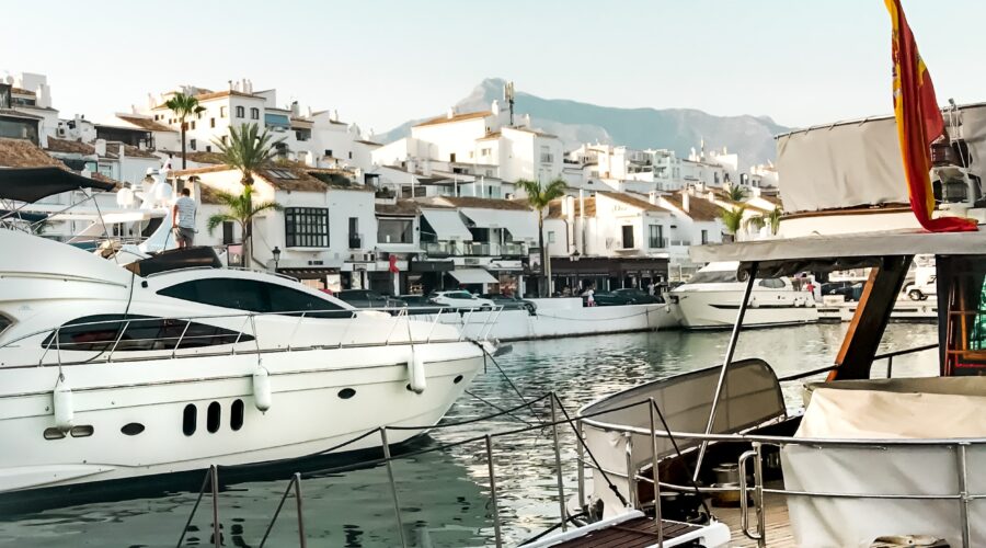 A view of a boat dock with and older boat and a newer yacht. The view shows a beautiful, rustic village in a foreign country.